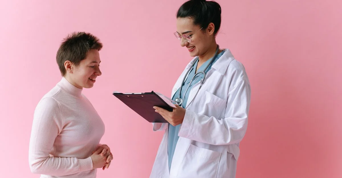 Un médico con bata blanca consulta a un paciente sonriente contra un fondo rosa.