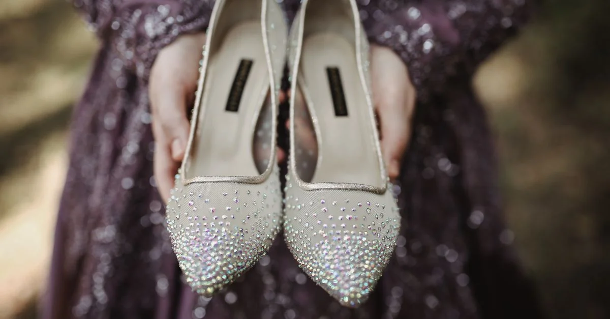Mujer con vestido de lentejuelas morado sosteniendo tacones brillantes al aire libre.