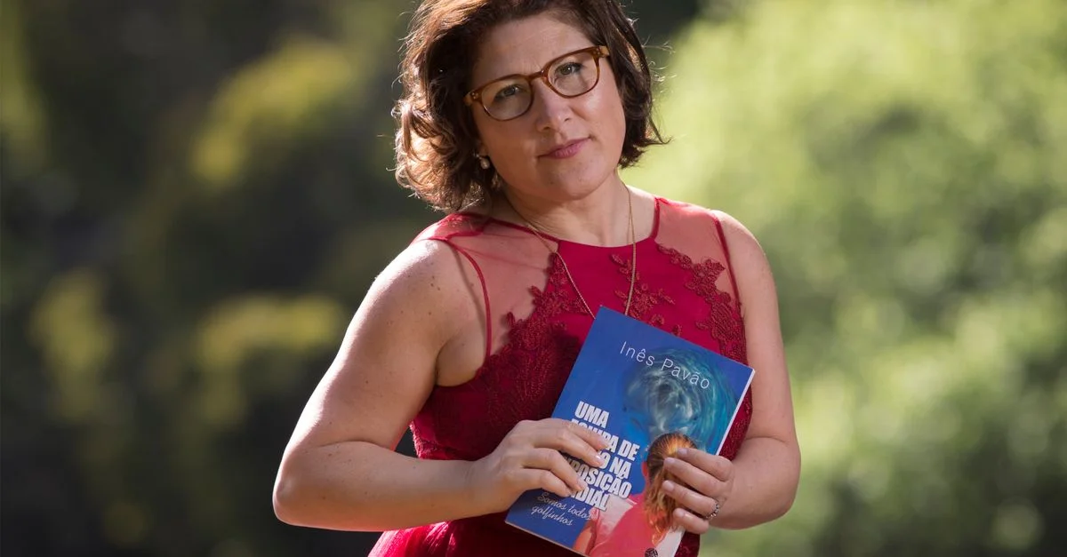 Una mujer con un vestido rojo sosteniendo un libro al aire libre en un parque soleado.