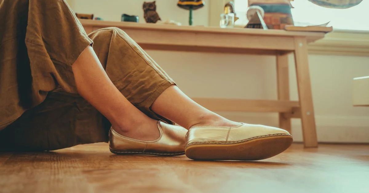 Un primer plano de piernas con zapatos cómodos tipo deslizables en interiores, que desprenden relajación y estilo.