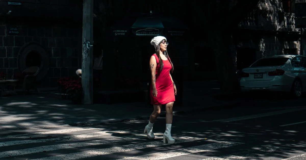 Mujer elegante con vestido rojo cruzando una calle de la ciudad durante el día, mostrando la moda urbana.