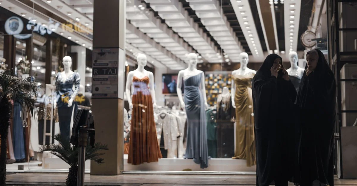 Exhibición de moda con maniquíes y compradores afuera de una tienda por la noche.